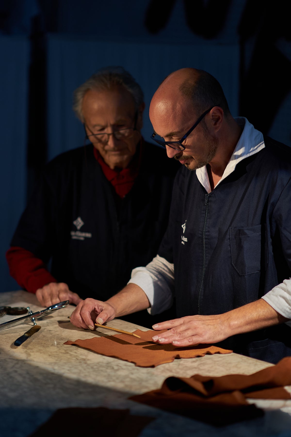 Alessandro and Gaetano Pellone aligning brown leather pieces on a marble table during the bespoke glove creation process